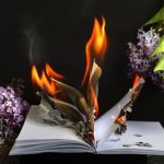 the book is burning with flames on a dark background with lilac flowers